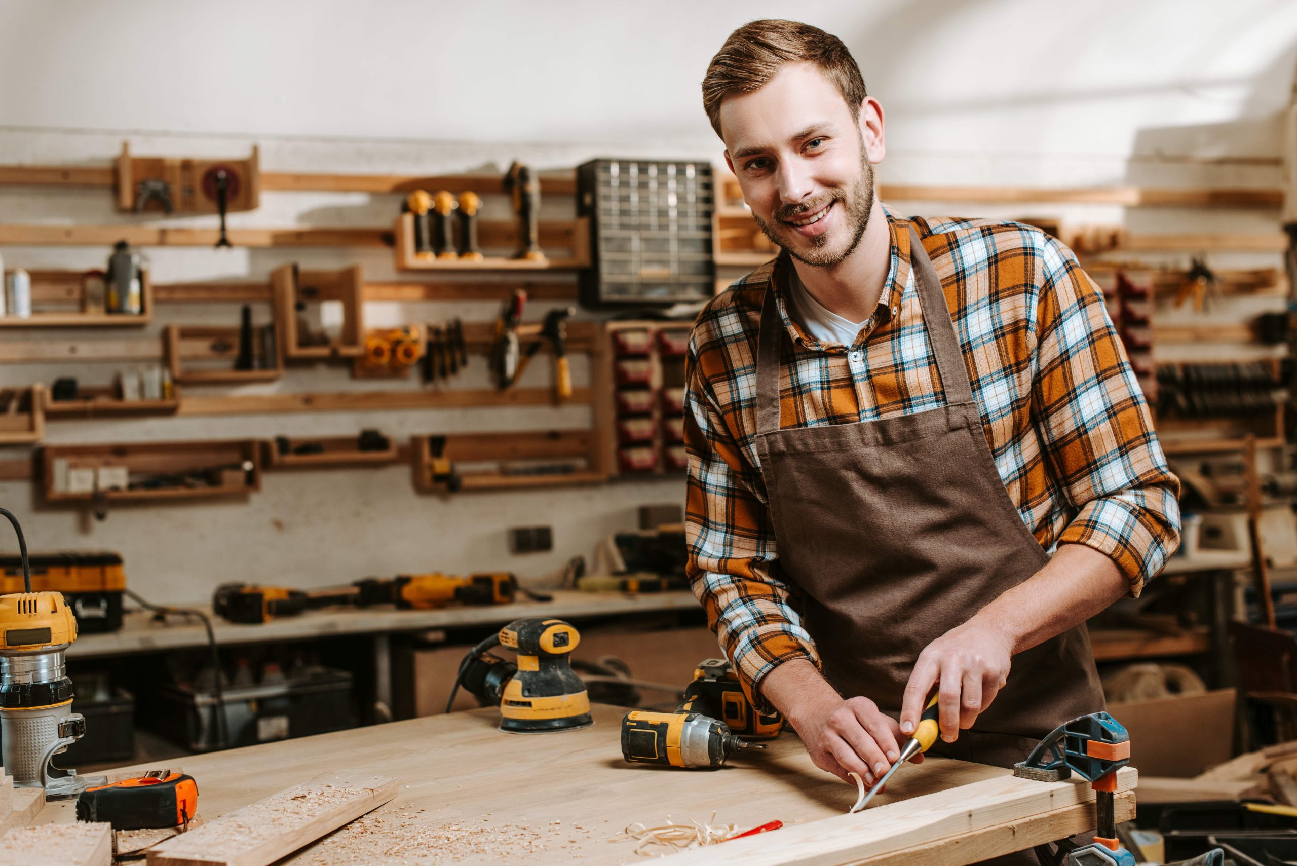 happy bearded carpenter carving wood in workshop Kleinunternehmer